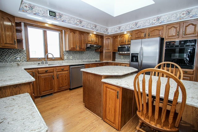 kitchen featuring black appliances, a kitchen island, light hardwood / wood-style floors, sink, and light stone counters