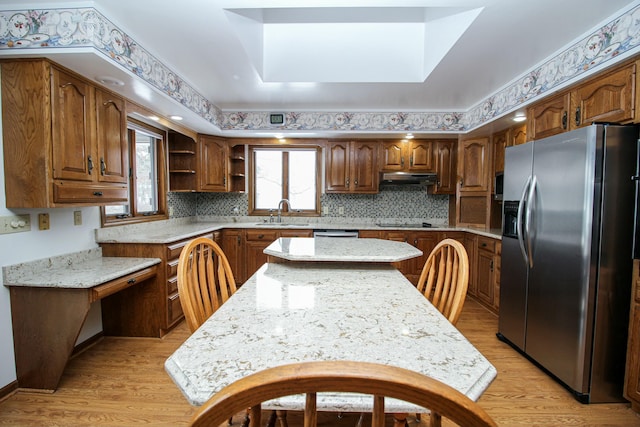 kitchen featuring stainless steel refrigerator with ice dispenser, sink, light stone counters, a center island, and light hardwood / wood-style floors