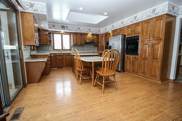 kitchen with a kitchen bar, stainless steel fridge with ice dispenser, sink, a kitchen island, and black oven