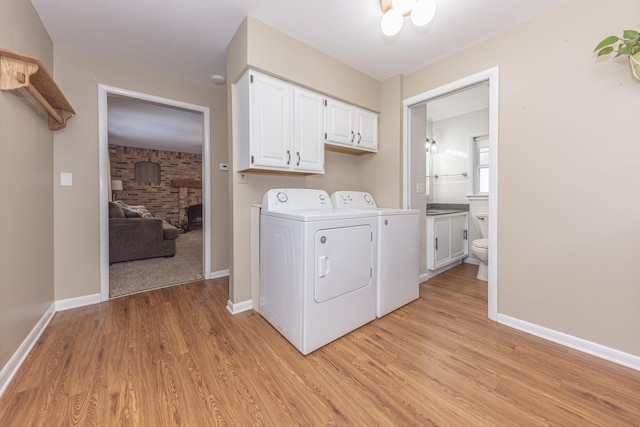 laundry room featuring washing machine and dryer, a brick fireplace, light hardwood / wood-style floors, and cabinets