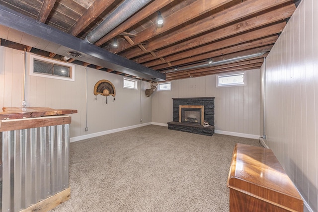 basement featuring light carpet, a fireplace, plenty of natural light, and wooden walls