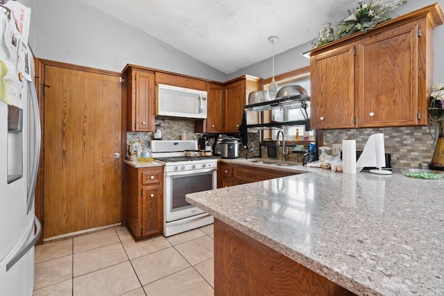 kitchen featuring decorative light fixtures, lofted ceiling, sink, light stone counters, and white appliances