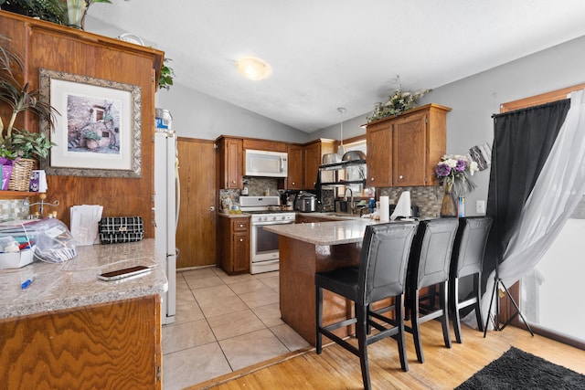 kitchen featuring lofted ceiling, sink, kitchen peninsula, pendant lighting, and white appliances