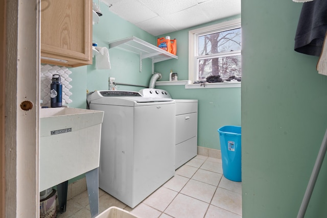 clothes washing area with cabinets, sink, washer and dryer, and light tile patterned floors