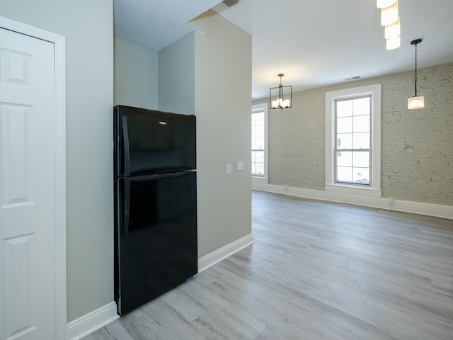 kitchen with black fridge, light hardwood / wood-style floors, hanging light fixtures, and a notable chandelier