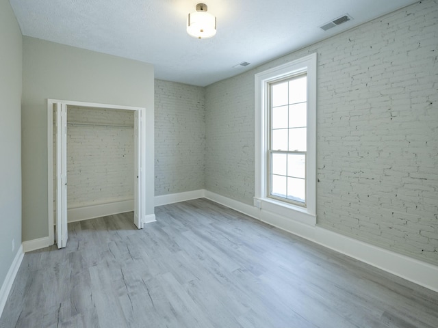 unfurnished bedroom with light hardwood / wood-style floors, a closet, a textured ceiling, and brick wall