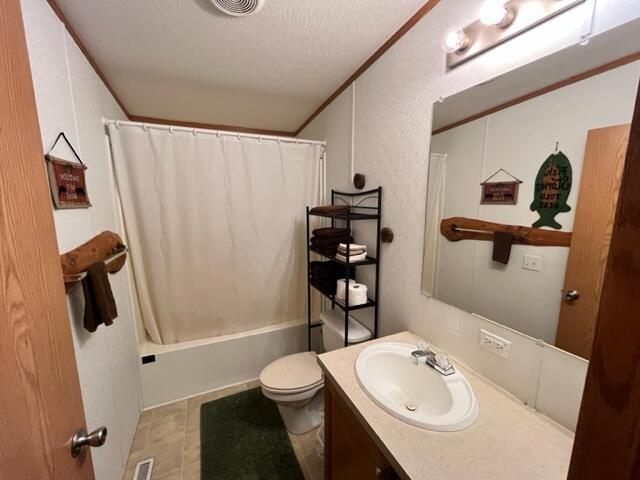 full bathroom with a textured ceiling, toilet, vanity, and shower / bath combo with shower curtain