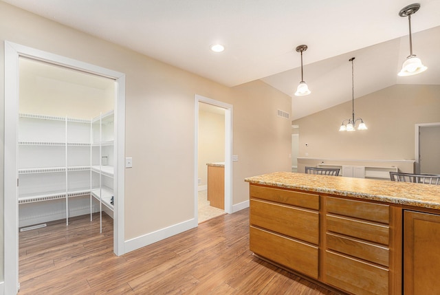 kitchen featuring decorative light fixtures, an inviting chandelier, light hardwood / wood-style floors, vaulted ceiling, and light stone counters