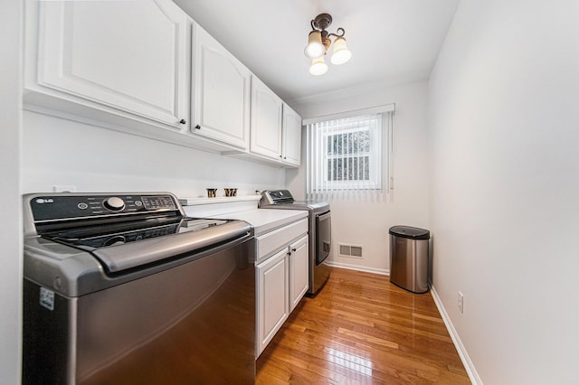 laundry area with cabinets, a notable chandelier, washer and dryer, and light wood-type flooring