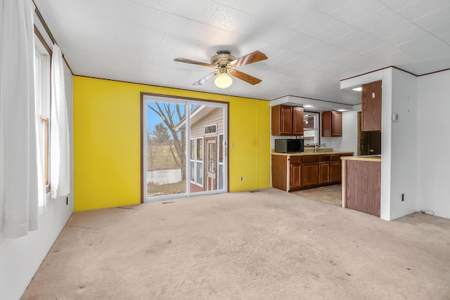 unfurnished living room with ceiling fan, light colored carpet, and sink