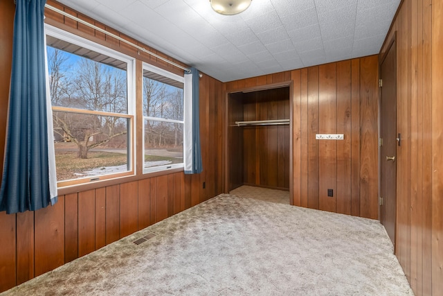 unfurnished bedroom featuring carpet flooring, wooden walls, and a closet