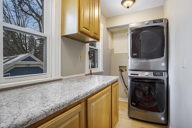 laundry area featuring a wealth of natural light, stacked washer and clothes dryer, light hardwood / wood-style flooring, and cabinets