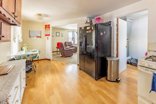 kitchen with black refrigerator with ice dispenser, white gas range, and light hardwood / wood-style flooring