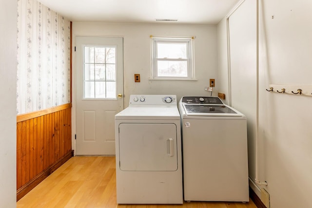 clothes washing area featuring separate washer and dryer, light hardwood / wood-style flooring, and wooden walls