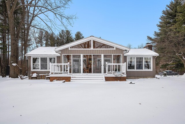 snow covered back of property with a sunroom