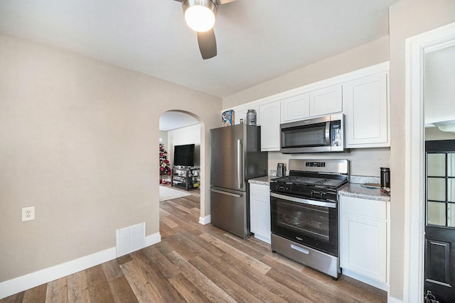 kitchen with hardwood / wood-style floors, white cabinets, stainless steel appliances, ceiling fan, and light stone counters