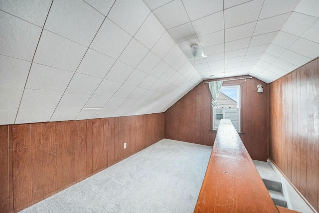 additional living space with vaulted ceiling, light carpet, and wood walls