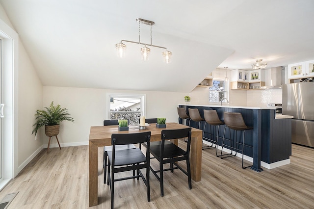 dining area with sink, light hardwood / wood-style floors, and vaulted ceiling