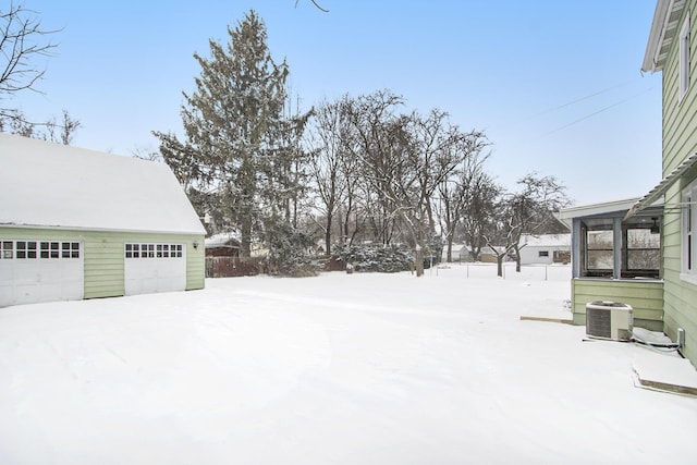 snowy yard with a garage, central AC unit, and an outbuilding