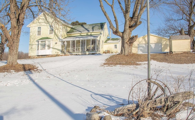 yard layered in snow with a garage, an outbuilding, and a sunroom