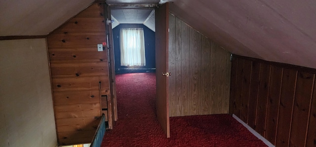 additional living space featuring vaulted ceiling, dark colored carpet, and wood walls