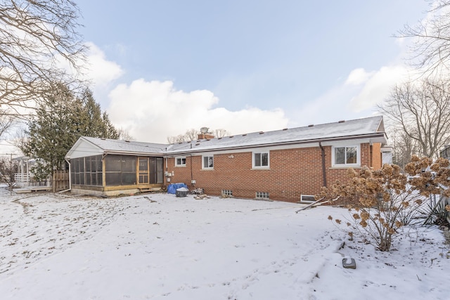 snow covered back of property with a sunroom