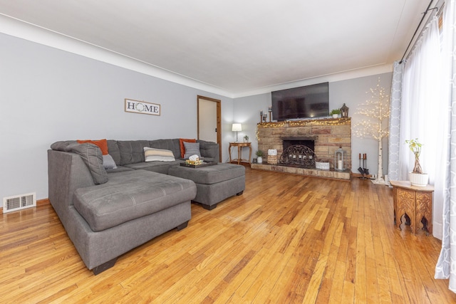 living room with light wood-type flooring, ornamental molding, and a fireplace