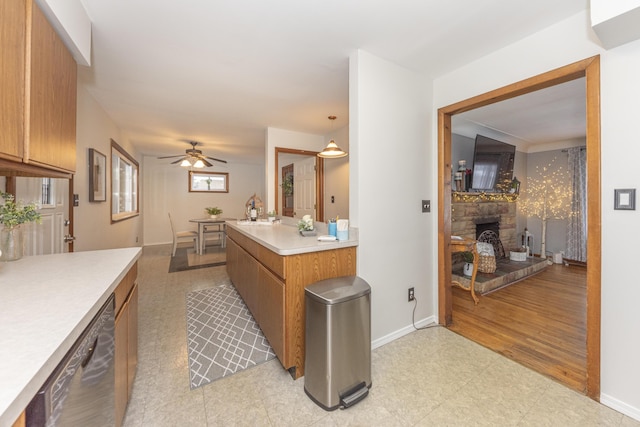 kitchen with ceiling fan, dishwasher, sink, hanging light fixtures, and a stone fireplace