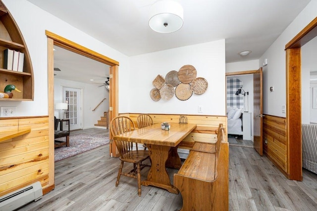 dining area with light hardwood / wood-style flooring, wood walls, and a baseboard heating unit