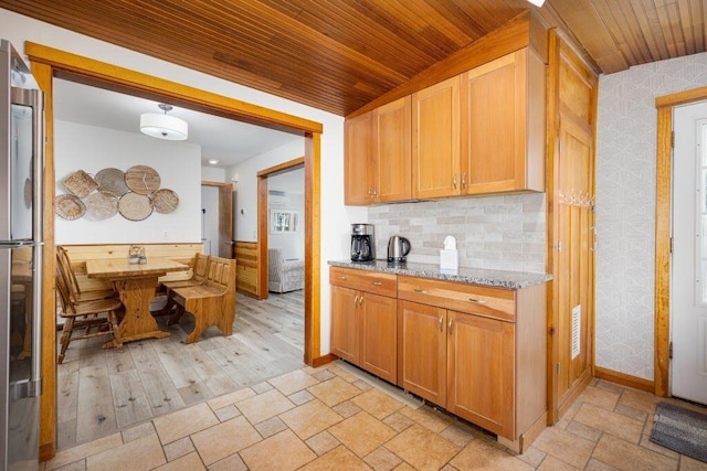 kitchen featuring decorative backsplash, light stone countertops, wooden ceiling, and fridge