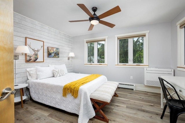 bedroom with ceiling fan, baseboard heating, hardwood / wood-style flooring, and wood walls