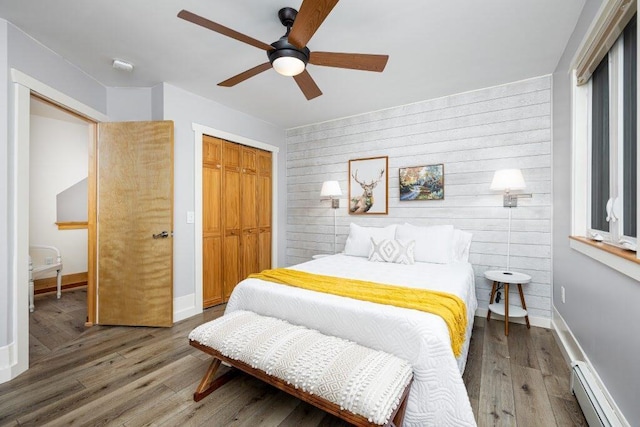 bedroom featuring hardwood / wood-style floors, a baseboard heating unit, wooden walls, a closet, and ceiling fan