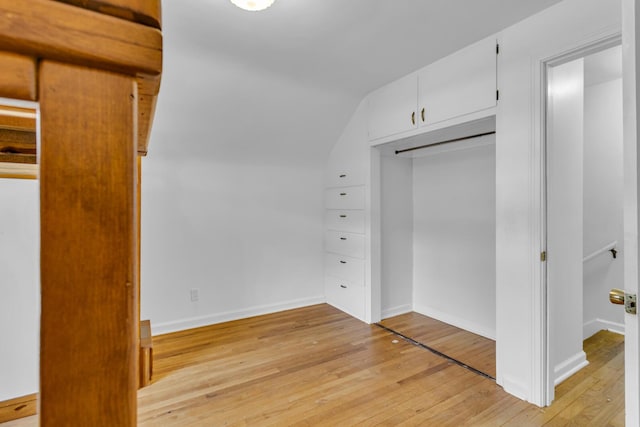 unfurnished bedroom featuring lofted ceiling, light wood-type flooring, and a closet