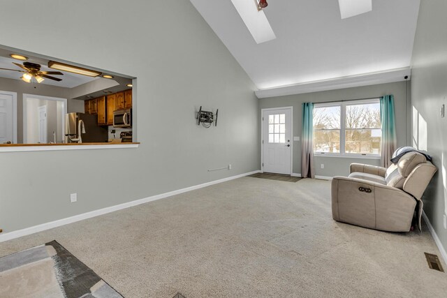 unfurnished living room featuring high vaulted ceiling, a skylight, light carpet, and ceiling fan