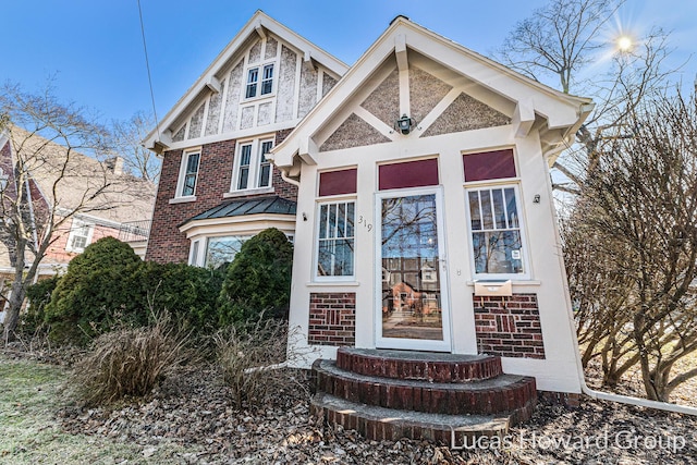 tudor home with a standing seam roof, brick siding, and metal roof