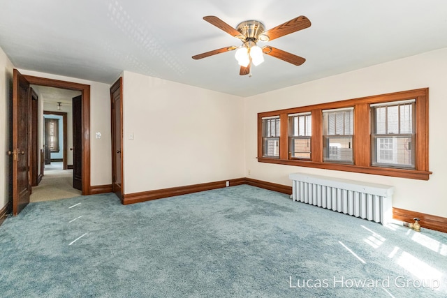 empty room with carpet flooring, radiator, a ceiling fan, and baseboards