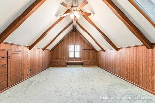 bonus room featuring lofted ceiling with beams, carpet floors, wooden walls, and a ceiling fan
