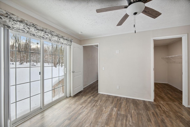 unfurnished bedroom featuring ceiling fan, a textured ceiling, a walk in closet, a closet, and dark hardwood / wood-style flooring