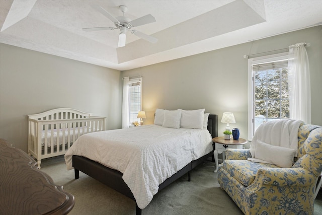 carpeted bedroom featuring ceiling fan and a tray ceiling