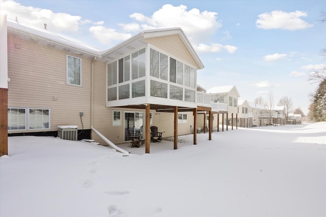 snow covered rear of property featuring a sunroom and central AC