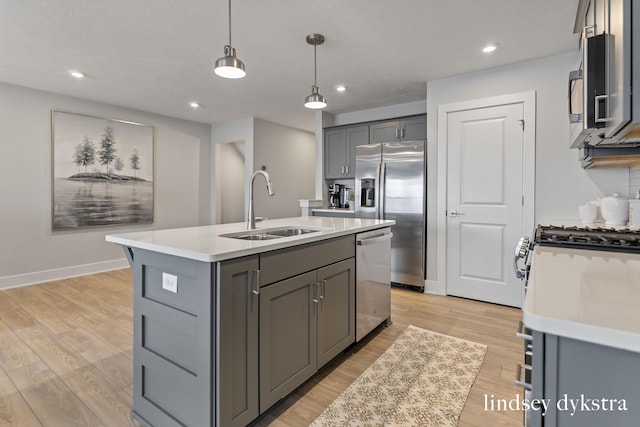 kitchen with pendant lighting, sink, appliances with stainless steel finishes, an island with sink, and gray cabinetry