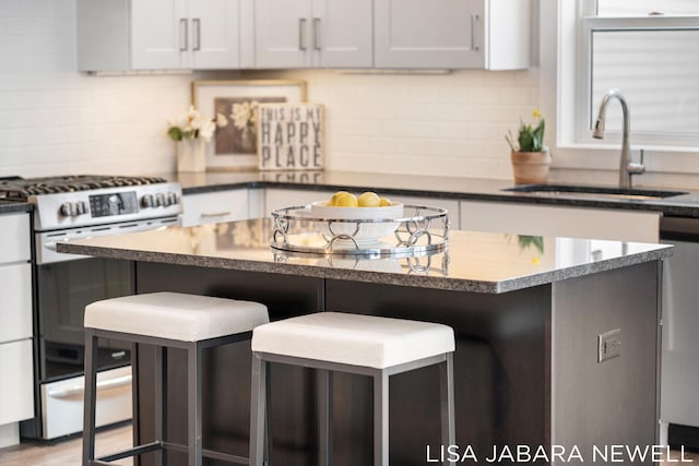 kitchen with a kitchen island, stainless steel range with gas cooktop, sink, a breakfast bar area, and white cabinets