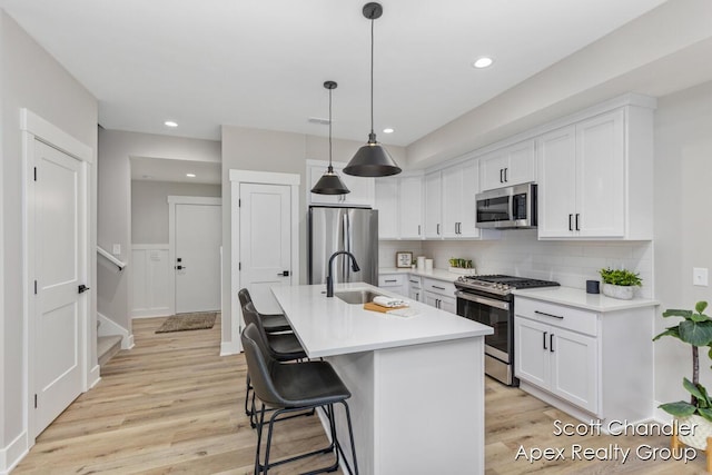 kitchen with a center island with sink, pendant lighting, sink, white cabinetry, and stainless steel appliances