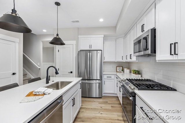 kitchen featuring stainless steel appliances, tasteful backsplash, pendant lighting, white cabinets, and sink