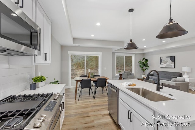 kitchen with decorative light fixtures, white cabinetry, stainless steel appliances, decorative backsplash, and sink