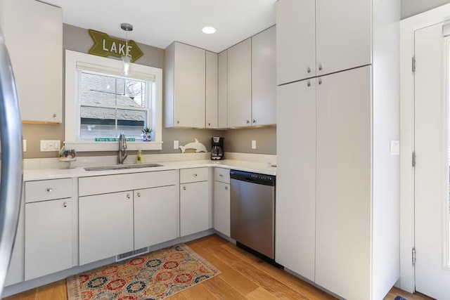 kitchen featuring appliances with stainless steel finishes, decorative light fixtures, white cabinetry, sink, and light hardwood / wood-style flooring