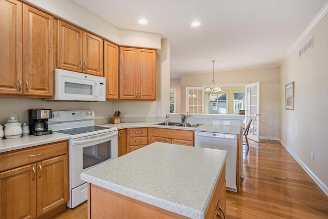 kitchen with sink, hanging light fixtures, a kitchen island, white appliances, and light hardwood / wood-style floors