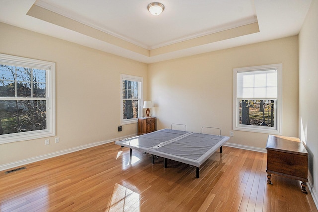 bedroom featuring a tray ceiling, ornamental molding, and light wood-type flooring