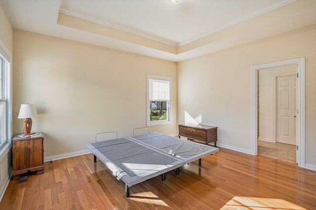 bedroom featuring a raised ceiling, ornamental molding, and light wood-type flooring