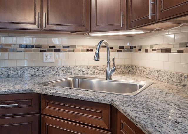 kitchen featuring sink, backsplash, dark brown cabinets, and light stone counters